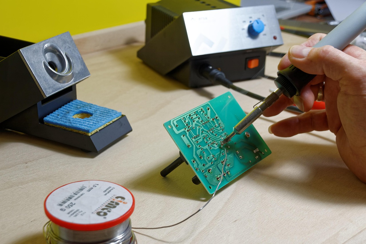 Hands soldering a green circuit board at a rework station